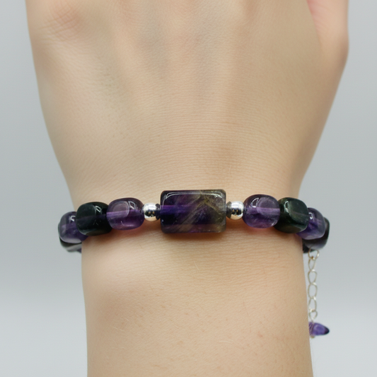 Bracelet with purple and black beads on a wrist against a neutral background