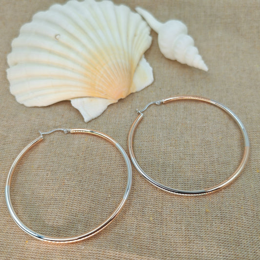 Two silver hoop earrings on a beige fabric background with two seashells.