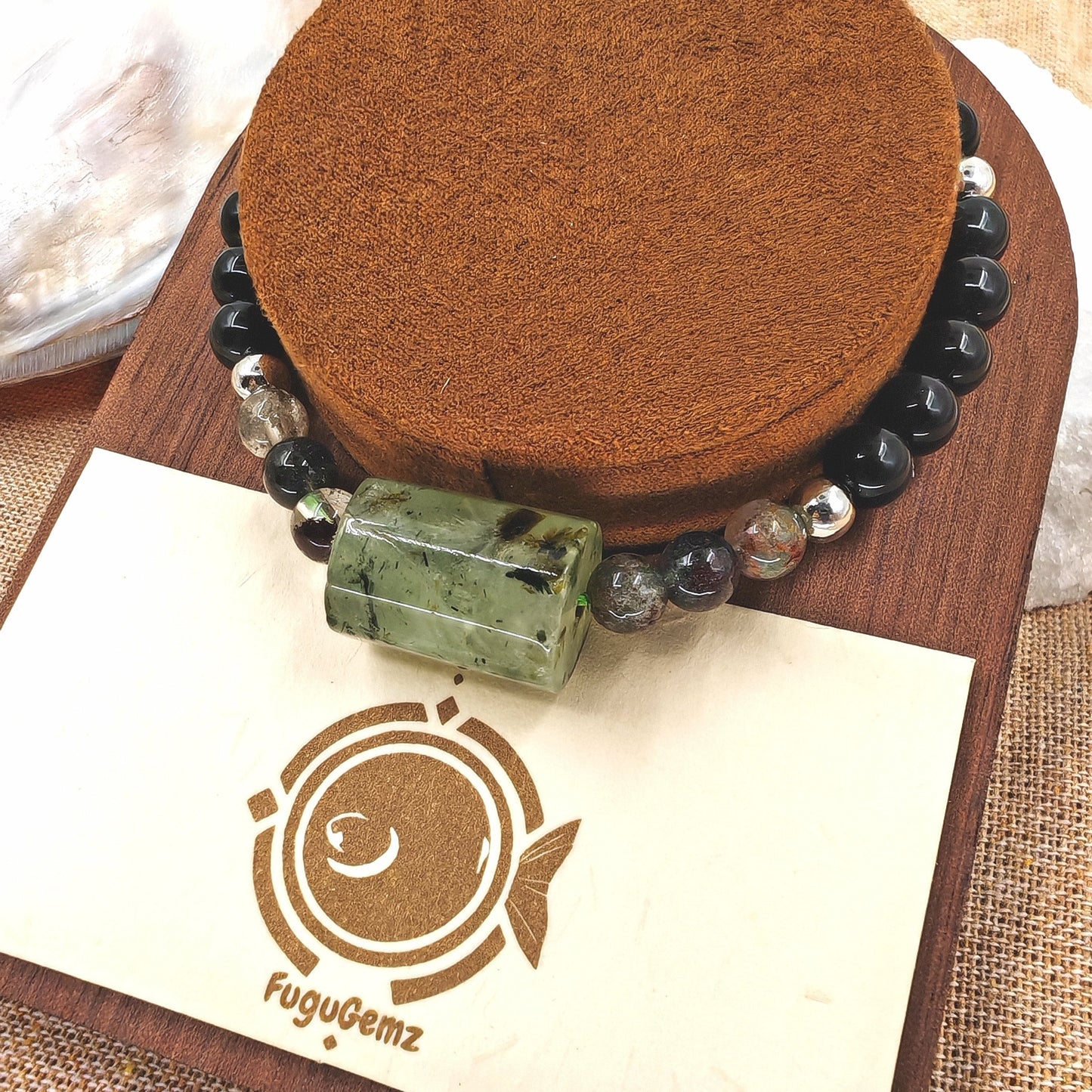 Close-up of rutilated quartz and obsidian beads with fugugemz logo