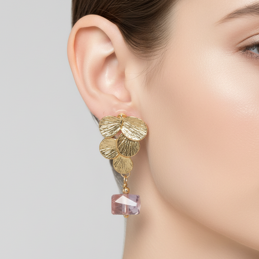 Gold leaf earring with a pink gemstone on a neutral background
