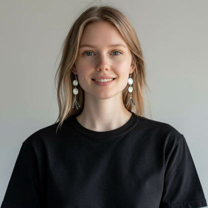 Woman wearing a black shirt with pearl earrings against a plain background