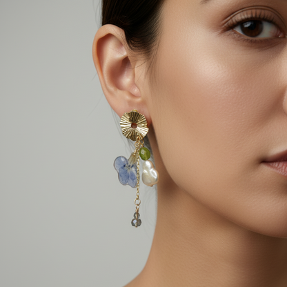Woman wearing gold dangle earrings with eternal flower, baroque pearl, olive quartz, and labradorite
