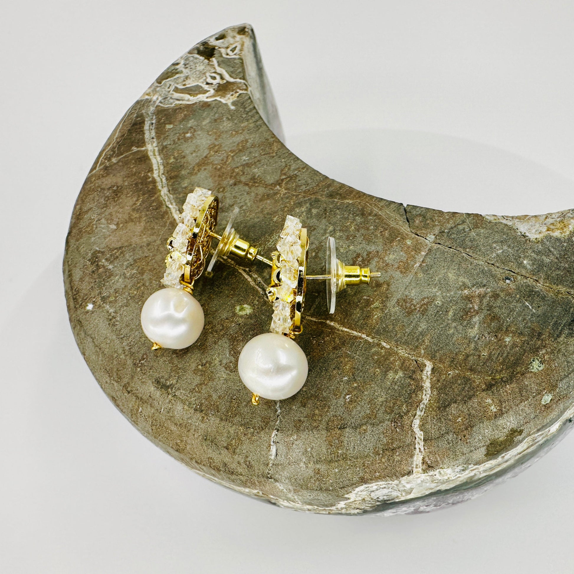 Pearl earrings with gold accents on a stone surface