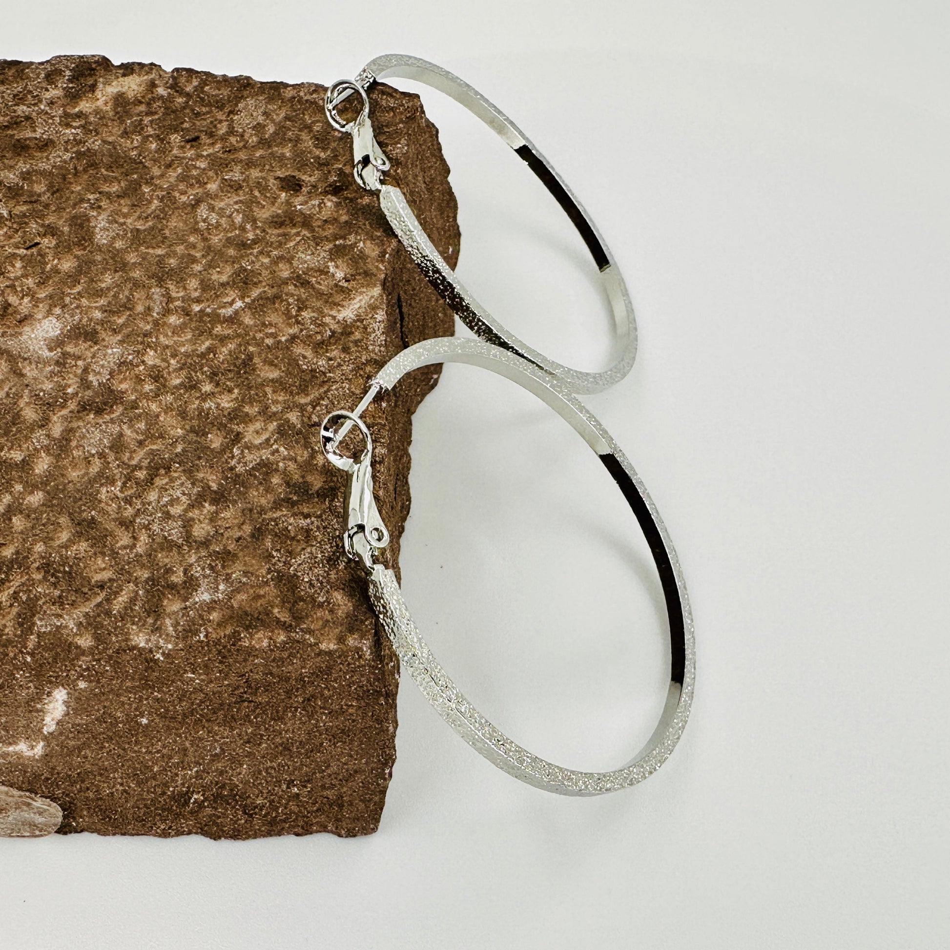 Silver hoop earrings on a textured stone surface