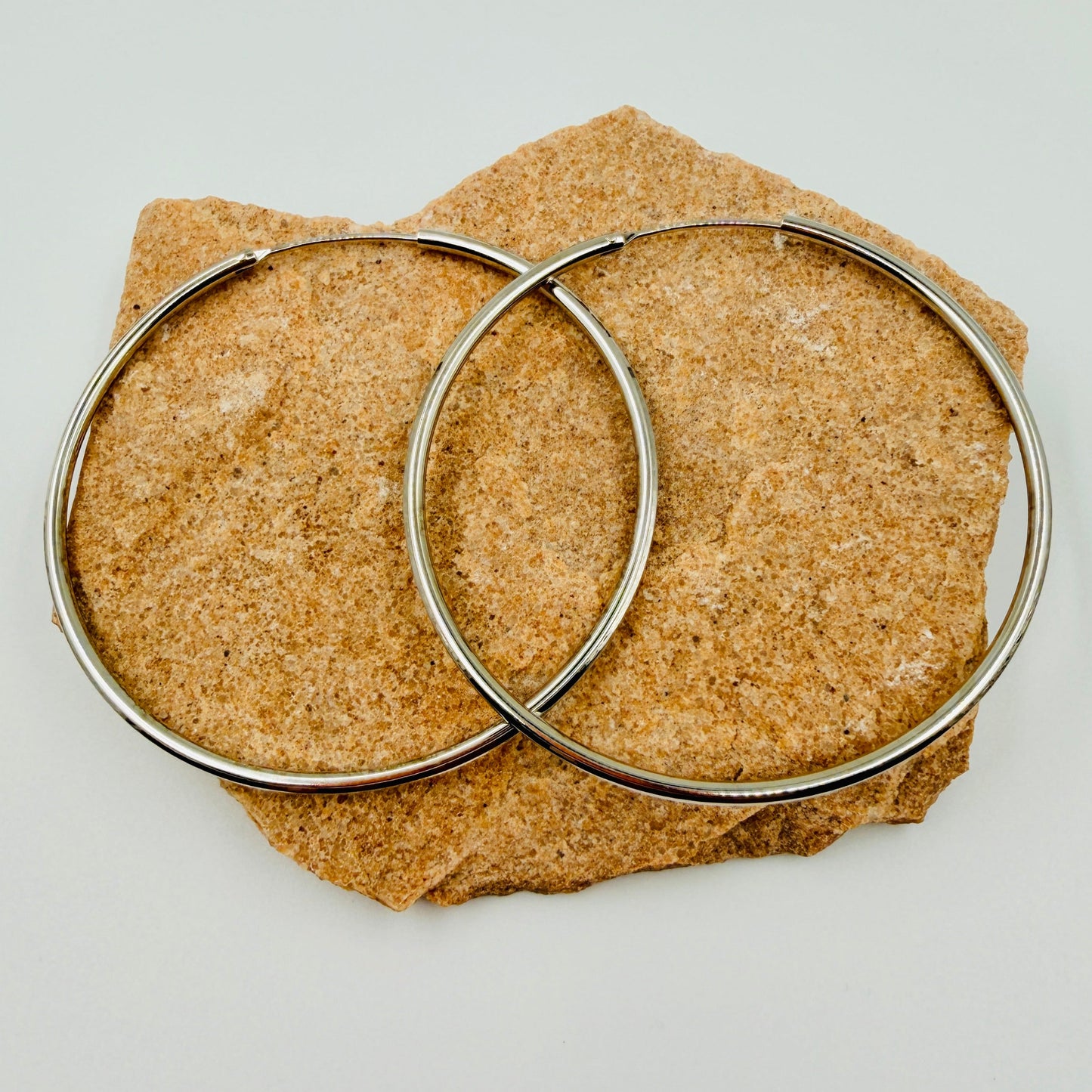 Two 50mm silver hoop earrings on a textured brown stone surface.