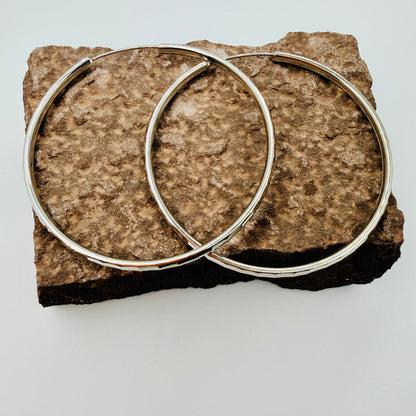 Two silver hoop earrings on a textured stone surface