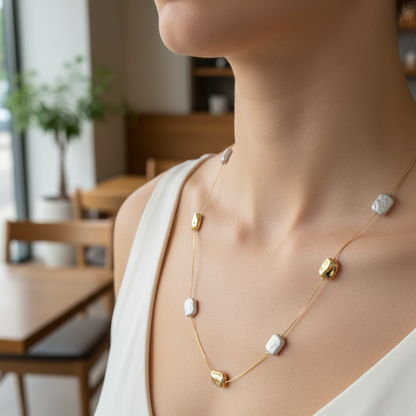 Woman wearing a delicate gold necklace with small pendants in a blurred indoor setting