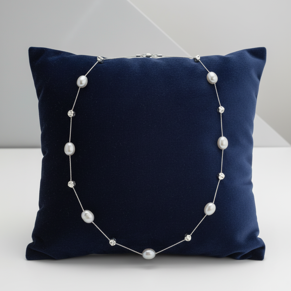 Navy blue pillow with a pearl necklace draped over it on a white background