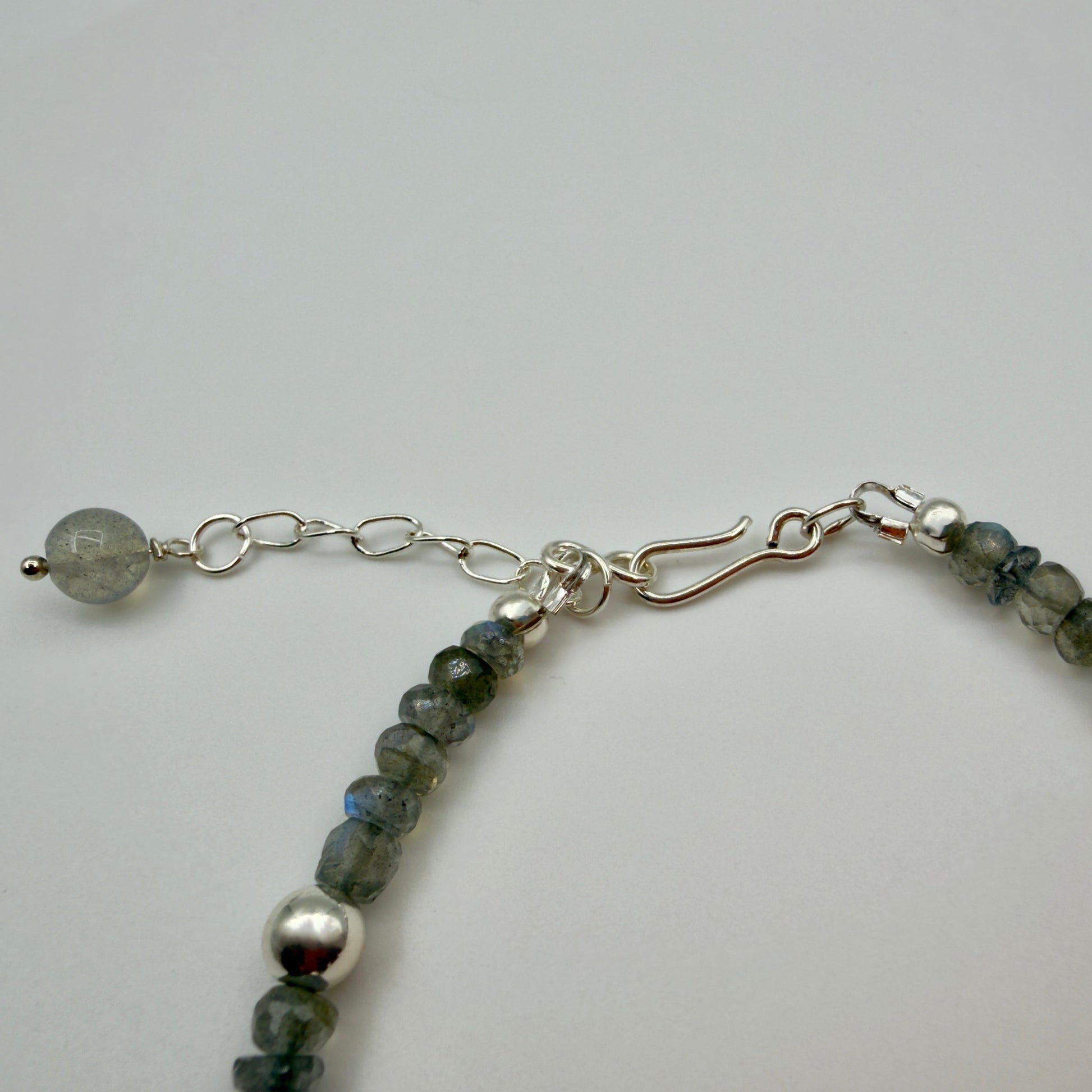 Close-up of a bracelet with green beads and silver chain on a light gray background