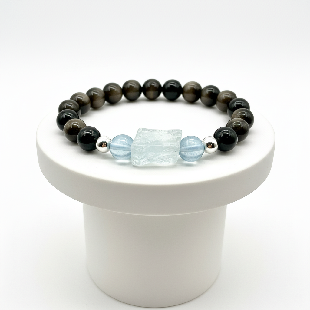Beaded bracelet with obsidian and light blue aquamarine on a white pedestal