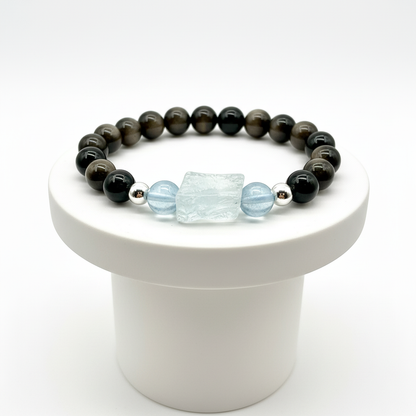 Beaded bracelet with obsidian and light blue aquamarine on a white pedestal