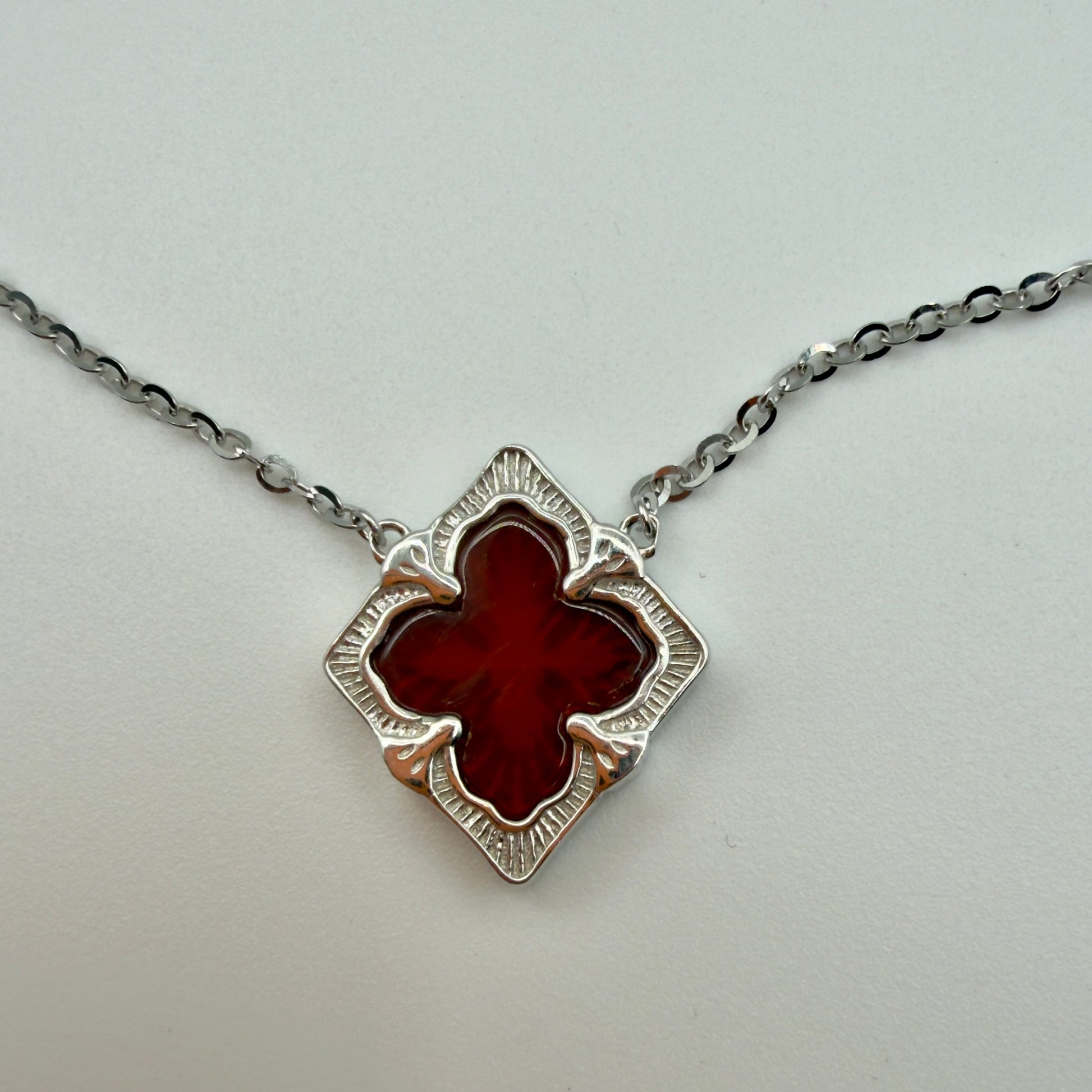Silver necklace with a red clover-shaped pendant on a light gray background