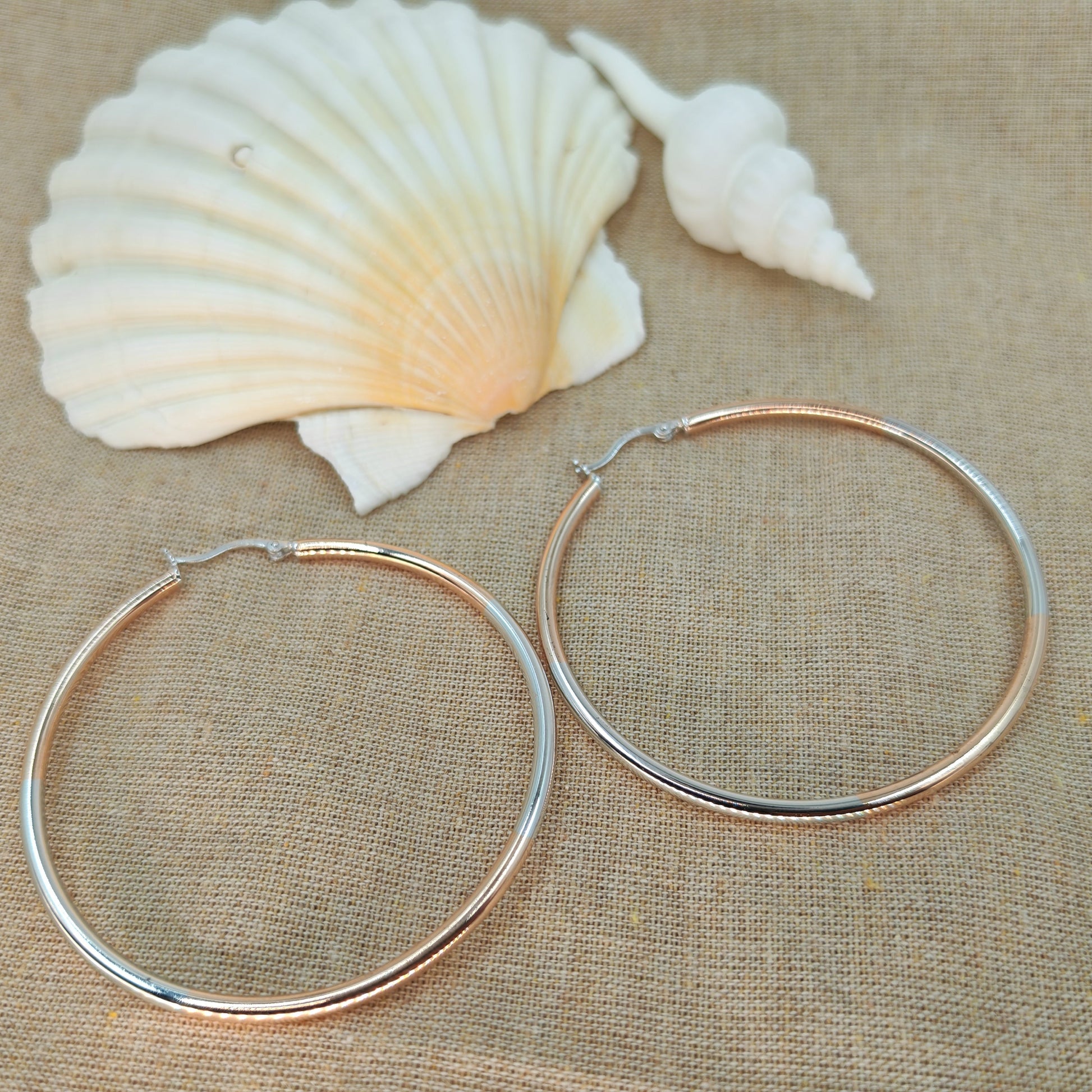 Two silver hoop earrings on a beige fabric background with two seashells.