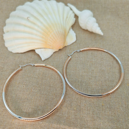 Two silver hoop earrings on a beige fabric background with two seashells.