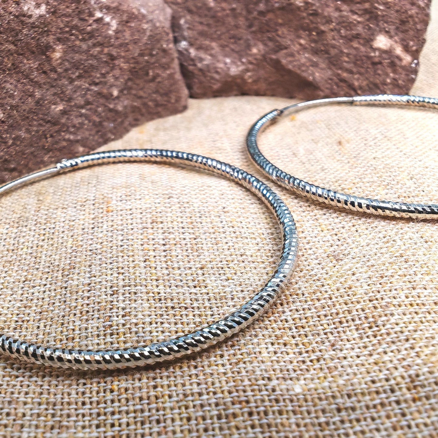 Two silver bangles on a textured surface with a stone background
