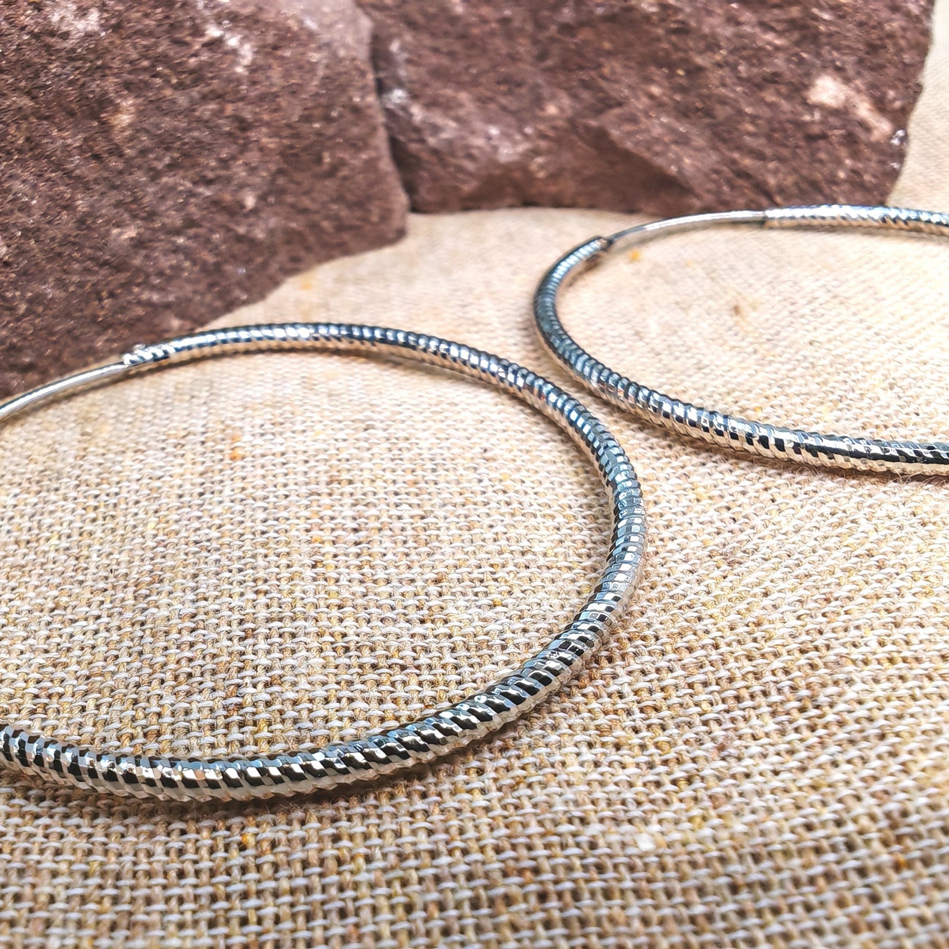 Two silver bangles on a textured surface with a stone background