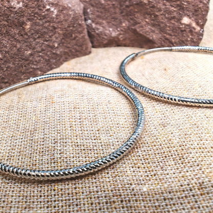 Two silver bangles on a textured surface with a stone background