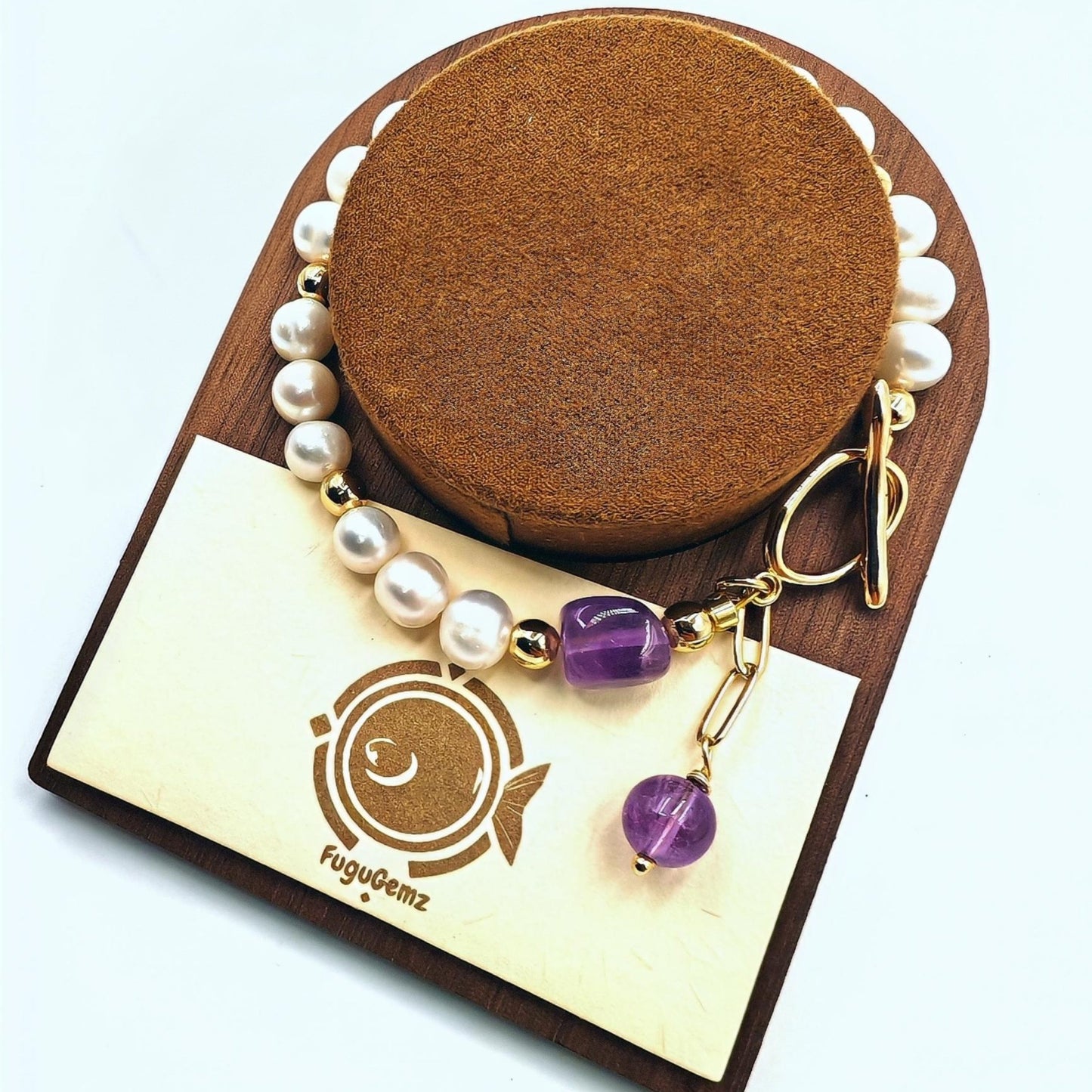 Bracelet with purple beads and gold accents on a wooden stand with a branded card underneath.