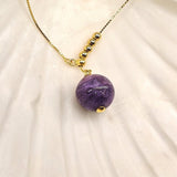 Close-up of charoite pendant and gold beads
