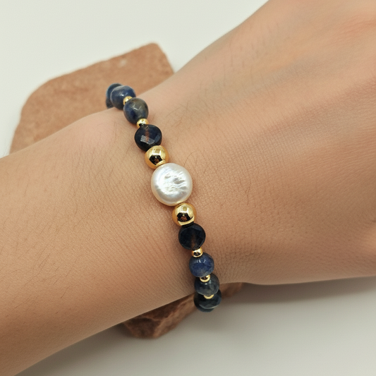 Bracelet with black beads and a pearl on a wrist against a neutral background
