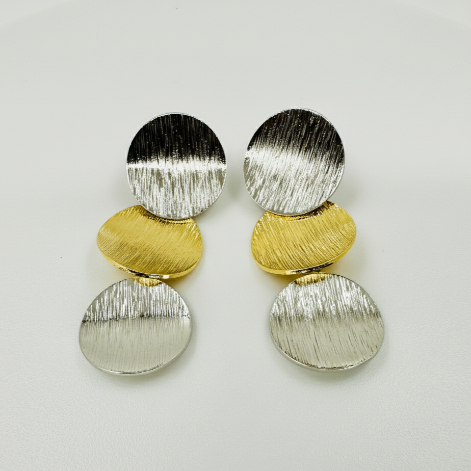 Pair of earrings with gold and silver circular designs on a light gray background
