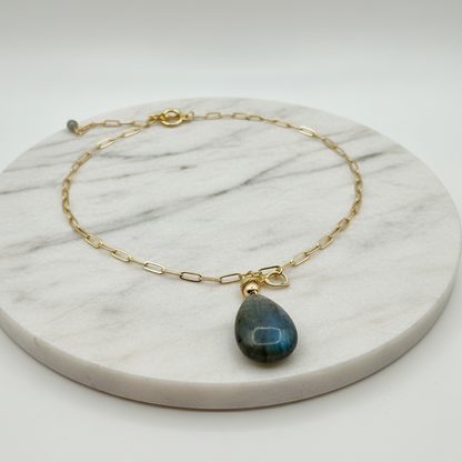 Gold bracelet with a blue teardrop pendant on a marble surface