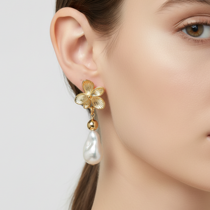 Gold flower-shaped earring with a pearl drop worn by a model on a white background