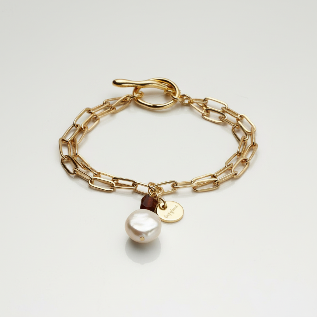 Gold chain bracelet with a pearl charm on a light gray background