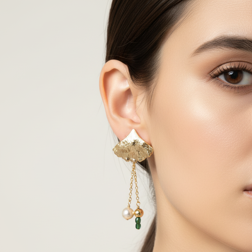 Close-up of a woman wearing gold earrings with green gemstones on a neutral background