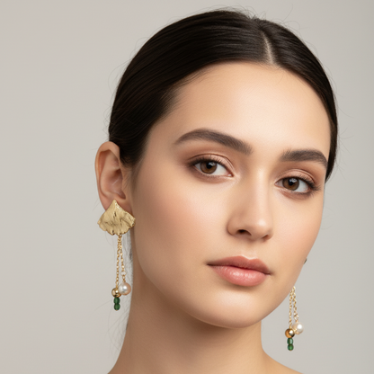 Woman wearing gold earrings with green gemstones against a neutral background