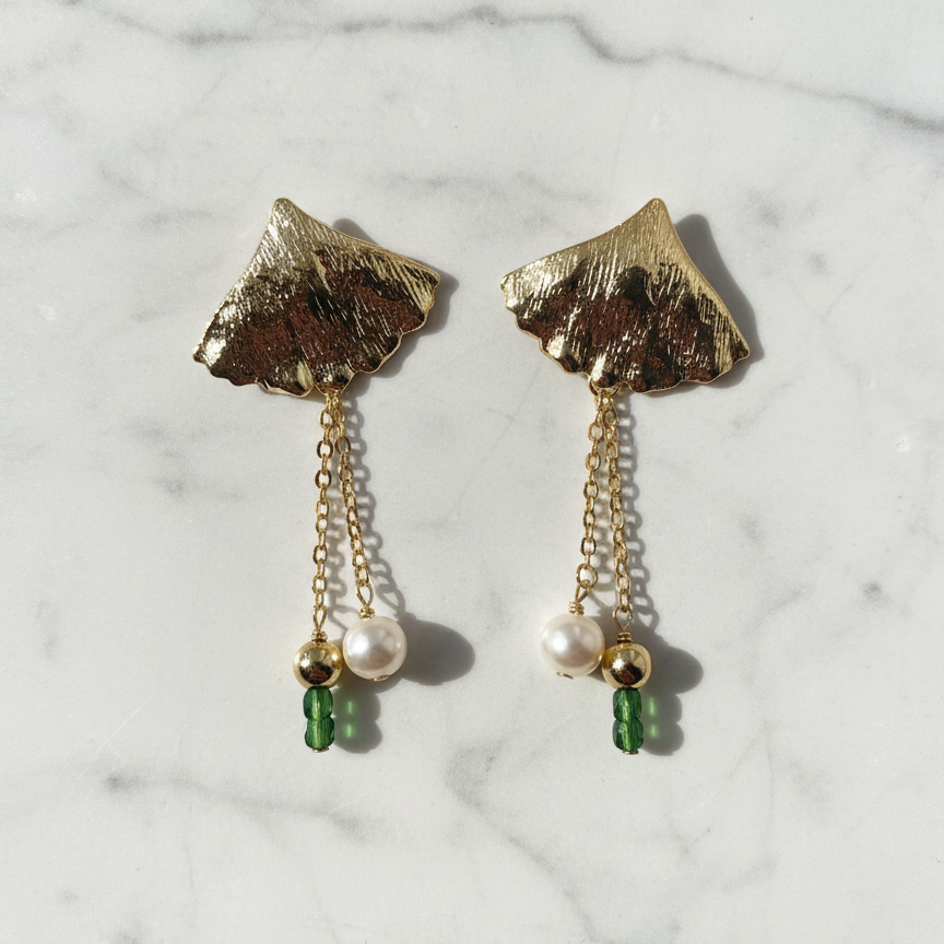 Gold leaf earrings with pearl and green gemstone drops on a marble background
