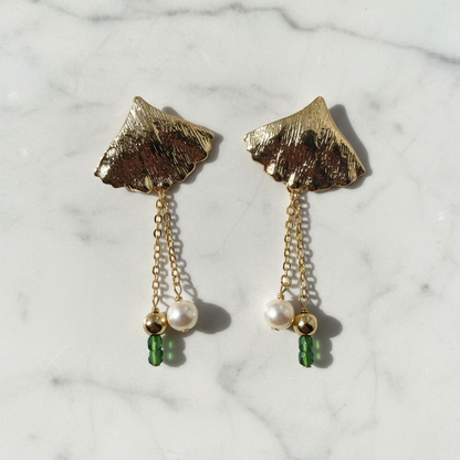 Gold leaf earrings with pearl and green gemstone drops on a marble background